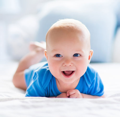 Smiling baby lying on tummy during infant care tummy time