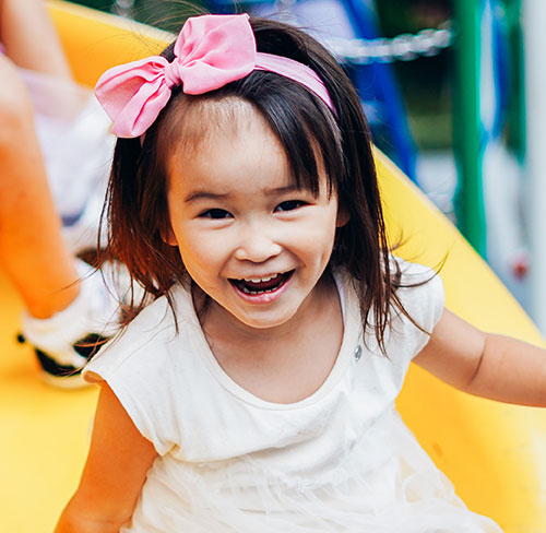 Smiling young girl sliding down a yellow slide on the outdoor playground