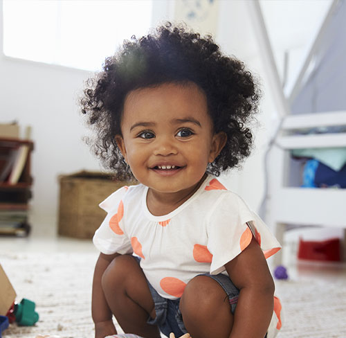 Smiling toddler girl crouching and playing in a bright daycare classroom